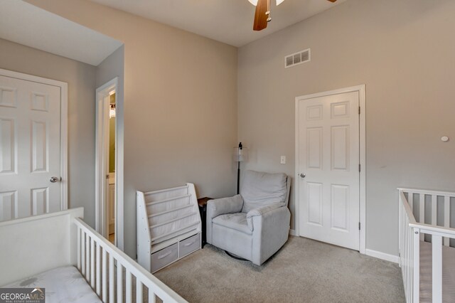 carpeted bedroom with ceiling fan and a nursery area