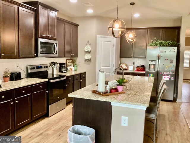 kitchen featuring light hardwood / wood-style floors, appliances with stainless steel finishes, and a center island with sink