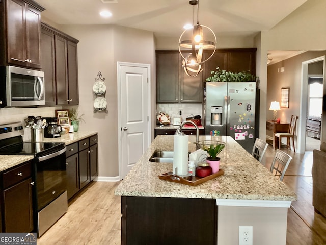 kitchen featuring pendant lighting, light wood-type flooring, an island with sink, decorative backsplash, and stainless steel appliances