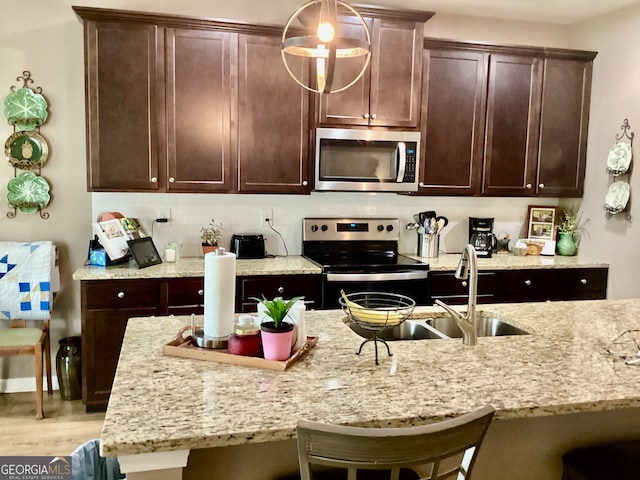 kitchen with light stone counters, decorative light fixtures, stainless steel appliances, light wood-type flooring, and a kitchen bar