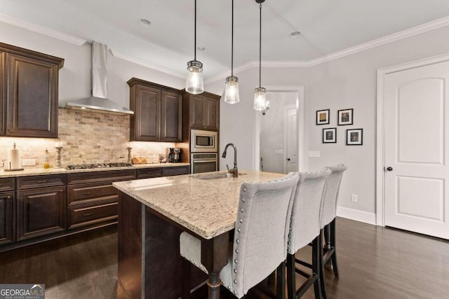 kitchen with sink, wall chimney range hood, pendant lighting, a center island with sink, and appliances with stainless steel finishes