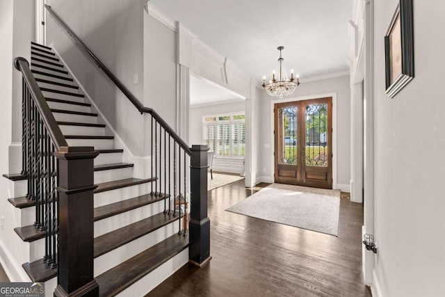 entryway with crown molding, french doors, dark wood-type flooring, and an inviting chandelier