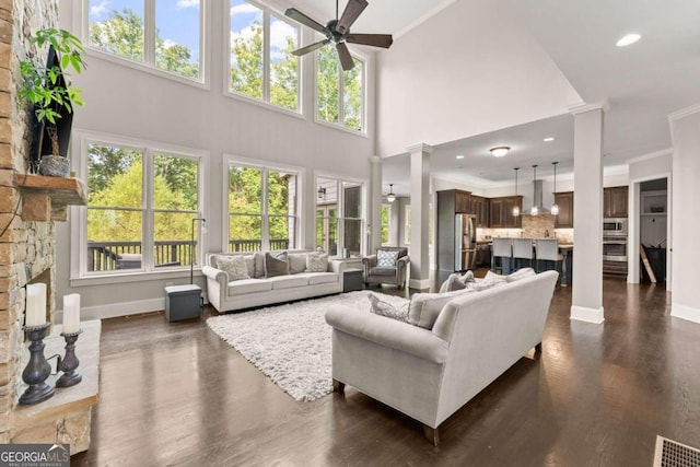 living room featuring ceiling fan, dark wood-type flooring, a stone fireplace, high vaulted ceiling, and ornamental molding