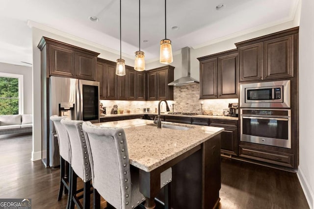 kitchen with sink, wall chimney range hood, decorative light fixtures, a center island with sink, and appliances with stainless steel finishes