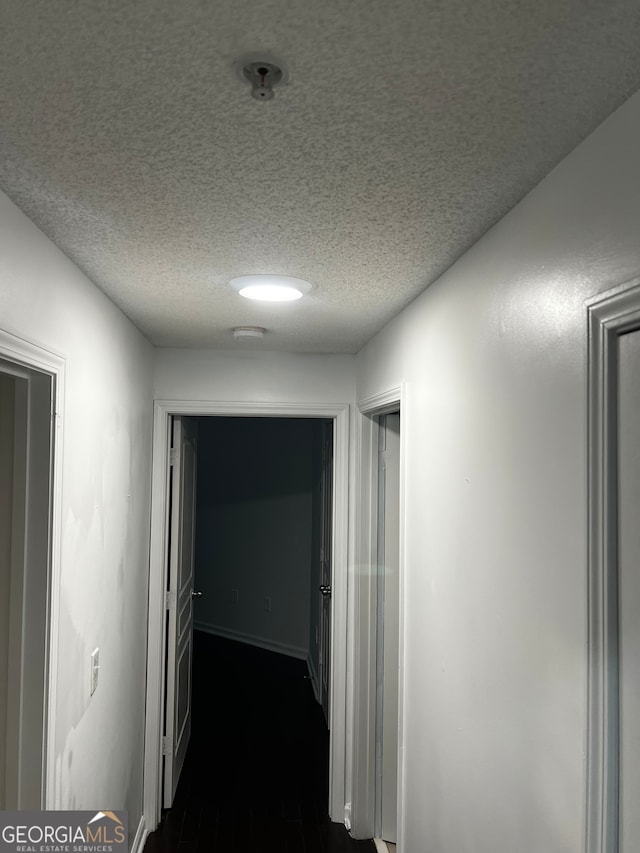 corridor with dark hardwood / wood-style flooring and a textured ceiling