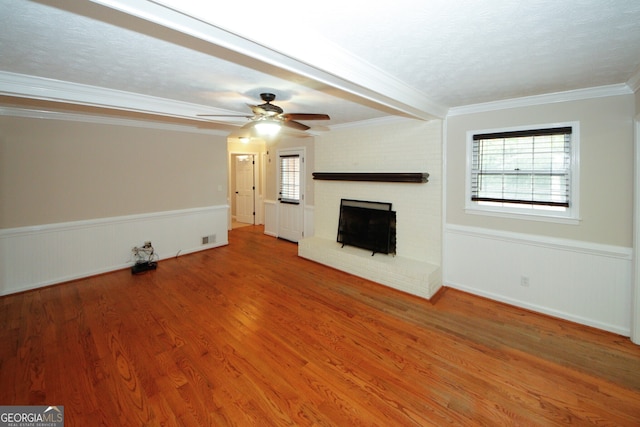 unfurnished living room featuring ceiling fan, wood-type flooring, crown molding, a fireplace, and a textured ceiling