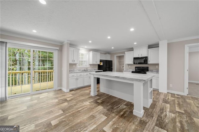 kitchen featuring light wood-type flooring, a center island, white cabinetry, and black appliances