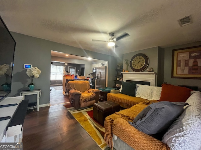 living room featuring ceiling fan, dark hardwood / wood-style floors, and a textured ceiling