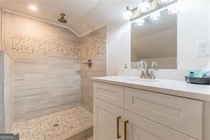 bathroom with vaulted ceiling, vanity, and tiled shower