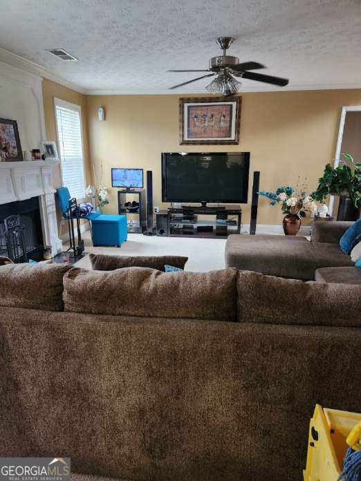 living room featuring a fireplace, a textured ceiling, crown molding, visible vents, and ceiling fan