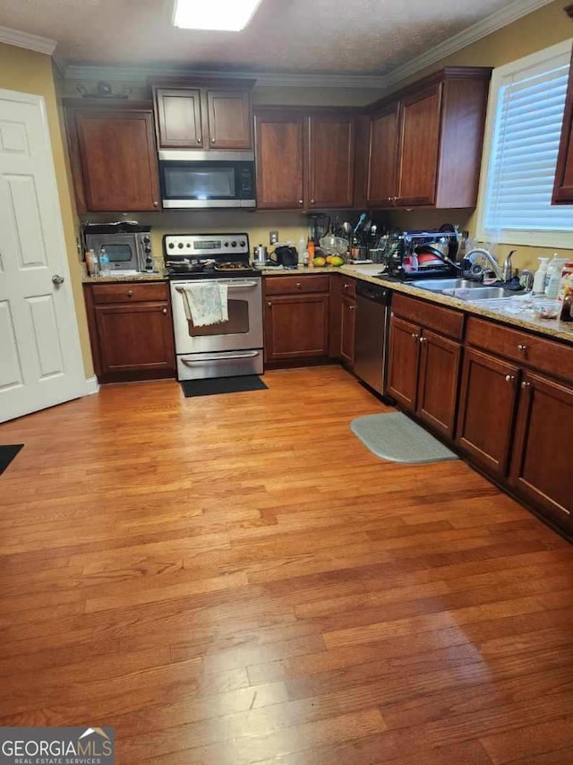 kitchen featuring sink, appliances with stainless steel finishes, light stone countertops, crown molding, and light hardwood / wood-style floors