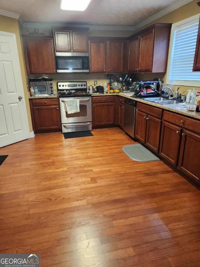 kitchen featuring stainless steel appliances, light wood-type flooring, a sink, and ornamental molding