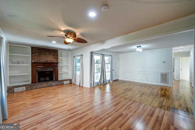 unfurnished living room with light hardwood / wood-style floors, built in shelves, ceiling fan, and a brick fireplace