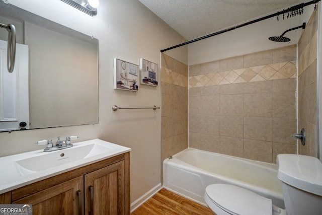 full bathroom with vanity, a textured ceiling, tiled shower / bath combo, hardwood / wood-style flooring, and toilet