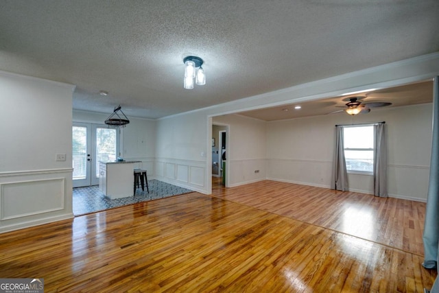 unfurnished living room with french doors, crown molding, hardwood / wood-style floors, and ceiling fan