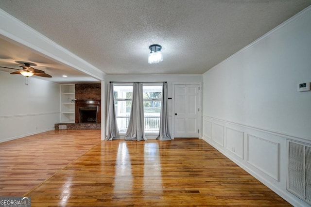 unfurnished living room featuring a textured ceiling, wood-type flooring, built in shelves, and a brick fireplace