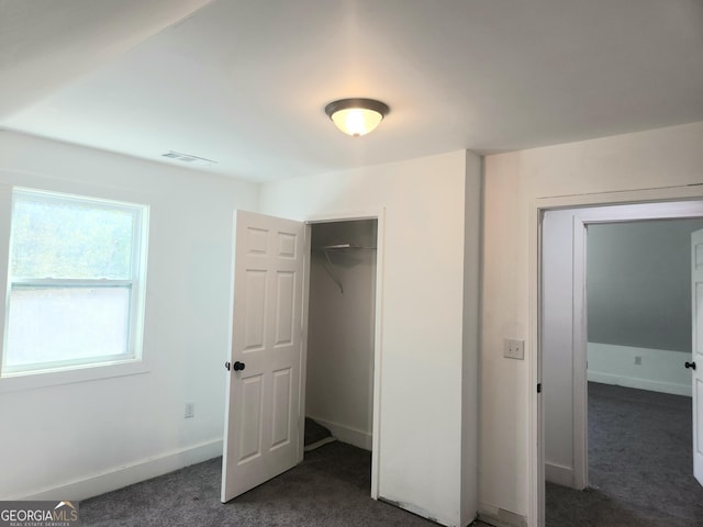 unfurnished bedroom with baseboards, visible vents, dark carpet, and a closet