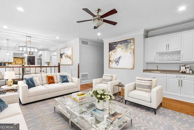 living room with crown molding, ceiling fan, light hardwood / wood-style flooring, and sink