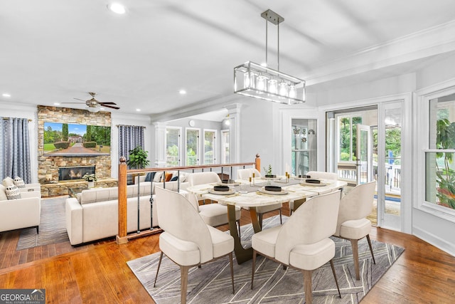 dining space featuring ceiling fan, ornamental molding, light hardwood / wood-style flooring, a fireplace, and ornate columns