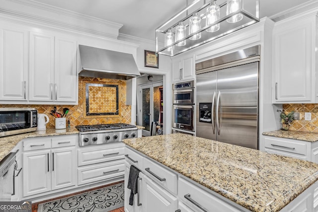 kitchen with appliances with stainless steel finishes, white cabinetry, and wall chimney range hood