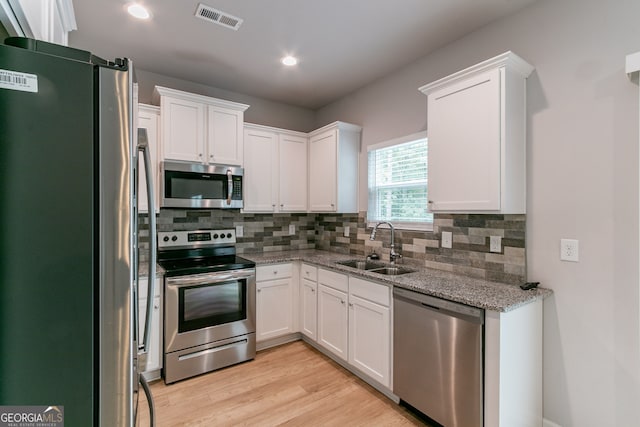 kitchen featuring sink, light stone countertops, appliances with stainless steel finishes, light hardwood / wood-style floors, and white cabinetry