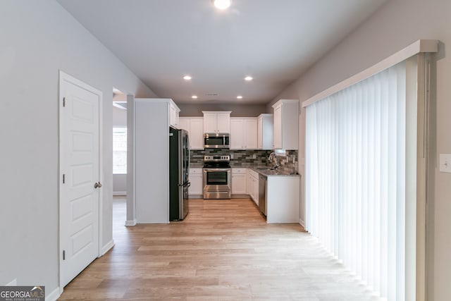 kitchen featuring white cabinets, sink, light wood-type flooring, appliances with stainless steel finishes, and tasteful backsplash