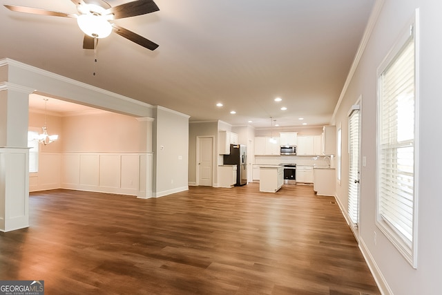 unfurnished living room featuring ceiling fan with notable chandelier, ornate columns, ornamental molding, dark hardwood / wood-style floors, and sink