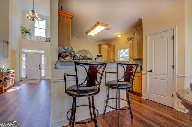 kitchen featuring dark wood-type flooring, light stone counters, a breakfast bar, kitchen peninsula, and an inviting chandelier