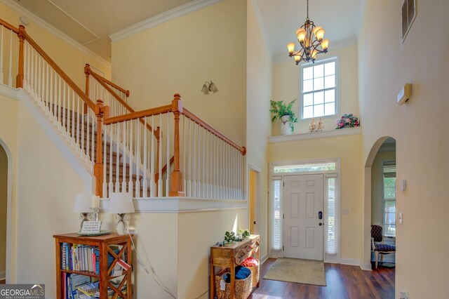 entryway with ornamental molding, a notable chandelier, dark wood-type flooring, and a high ceiling