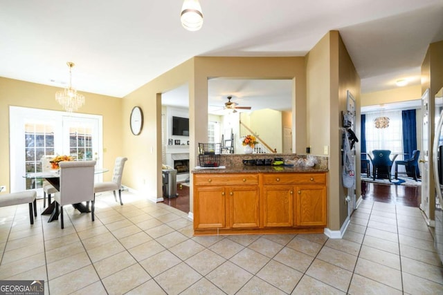 kitchen featuring ceiling fan with notable chandelier, hanging light fixtures, light tile patterned flooring, and dark stone counters