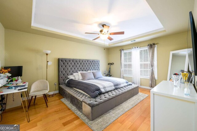 bedroom featuring ceiling fan, light wood-type flooring, and a tray ceiling