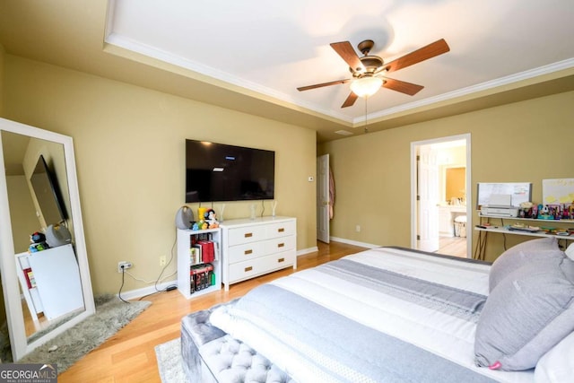 bedroom featuring a tray ceiling, light hardwood / wood-style flooring, ensuite bath, ornamental molding, and ceiling fan