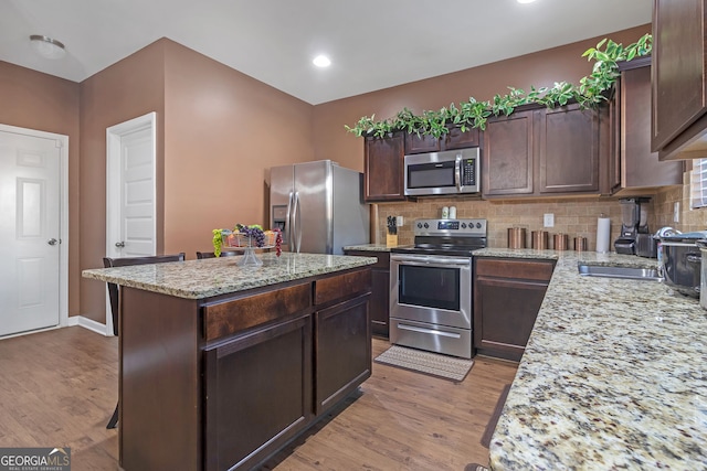 kitchen with light stone countertops, stainless steel appliances, a center island, and light hardwood / wood-style flooring