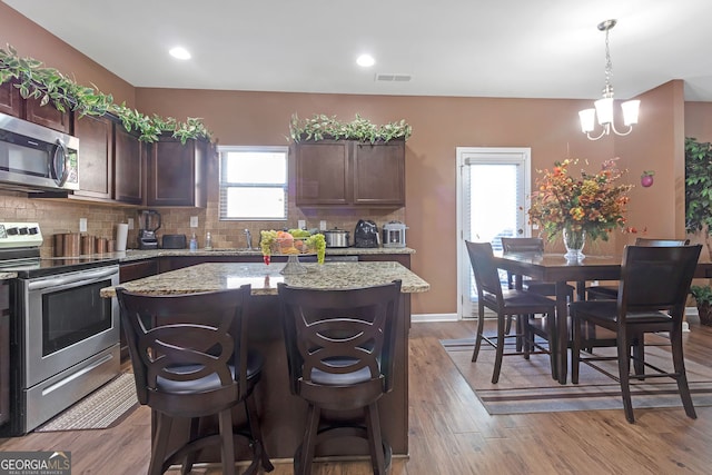 kitchen with pendant lighting, a kitchen island, appliances with stainless steel finishes, light wood-type flooring, and decorative backsplash