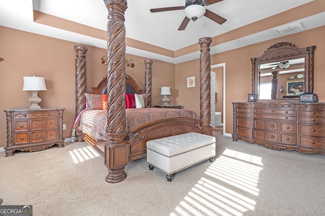 bedroom with a tray ceiling, ceiling fan, light colored carpet, and ensuite bathroom