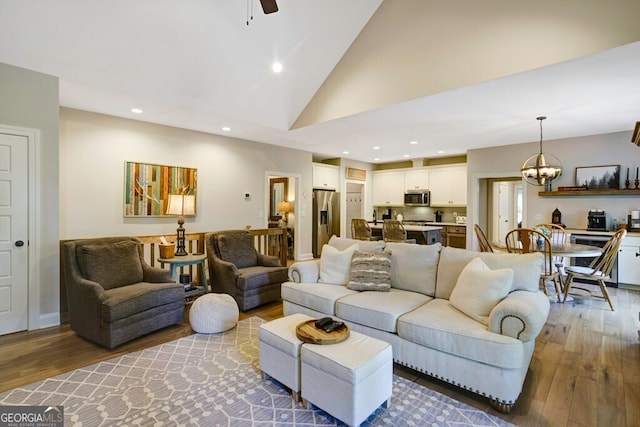 living room with high vaulted ceiling, ceiling fan with notable chandelier, and hardwood / wood-style flooring