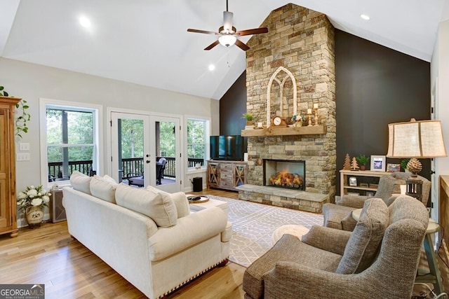 living room featuring high vaulted ceiling, a stone fireplace, ceiling fan, light hardwood / wood-style flooring, and french doors