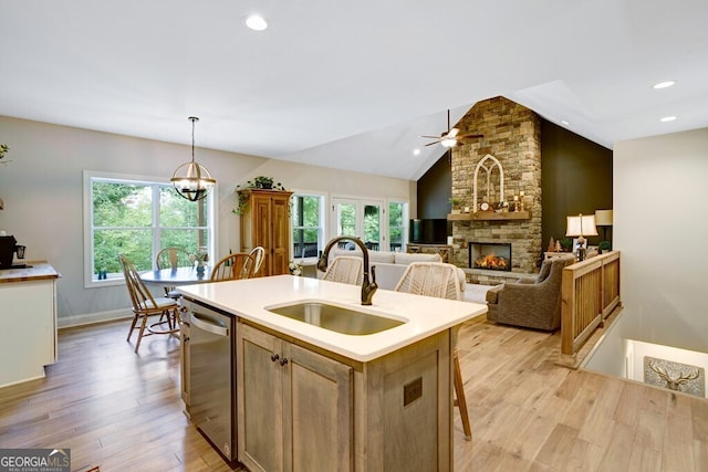 kitchen featuring hanging light fixtures, vaulted ceiling, an island with sink, stainless steel dishwasher, and sink