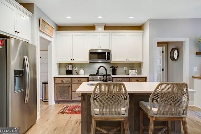 kitchen with white cabinetry, light hardwood / wood-style floors, appliances with stainless steel finishes, and a center island with sink