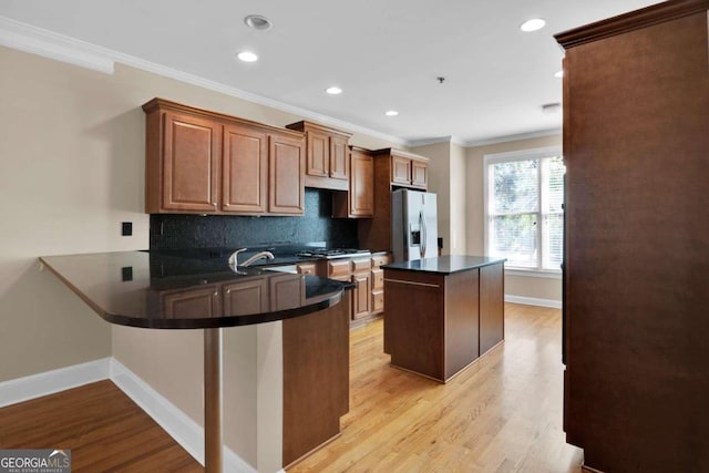 kitchen with stainless steel fridge, ornamental molding, kitchen peninsula, backsplash, and light wood-type flooring