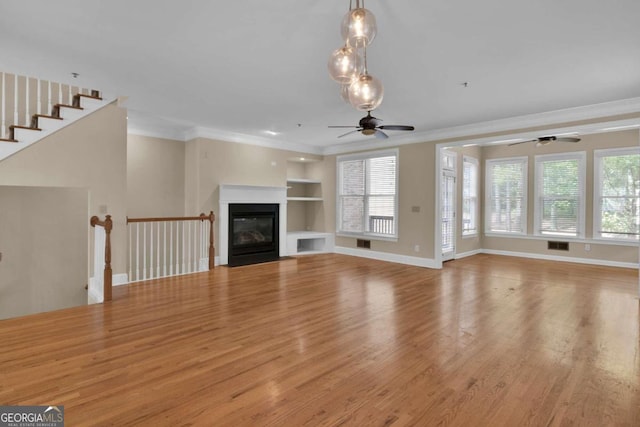 unfurnished living room with built in shelves, light hardwood / wood-style floors, ornamental molding, and ceiling fan