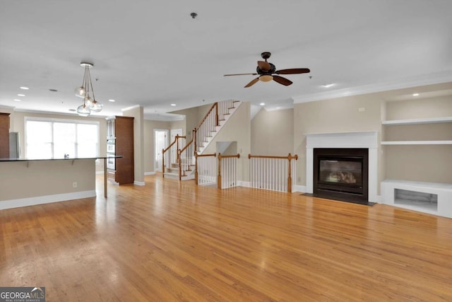 unfurnished living room featuring ceiling fan with notable chandelier, light wood-type flooring, crown molding, and built in features