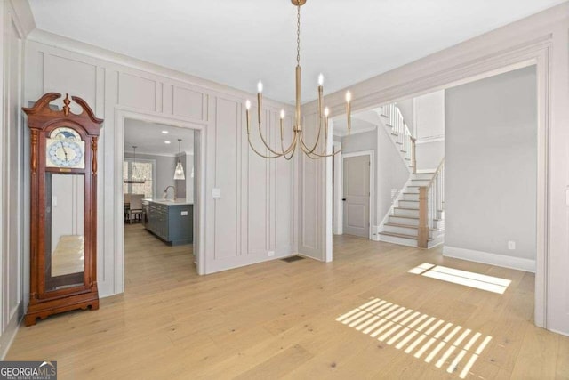 unfurnished dining area with crown molding, light hardwood / wood-style floors, and a notable chandelier