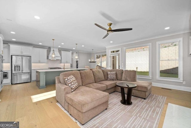 living room with ceiling fan, ornamental molding, plenty of natural light, and light hardwood / wood-style floors