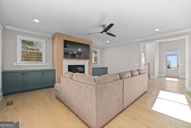 living room featuring light hardwood / wood-style flooring, a large fireplace, ceiling fan, and ornamental molding