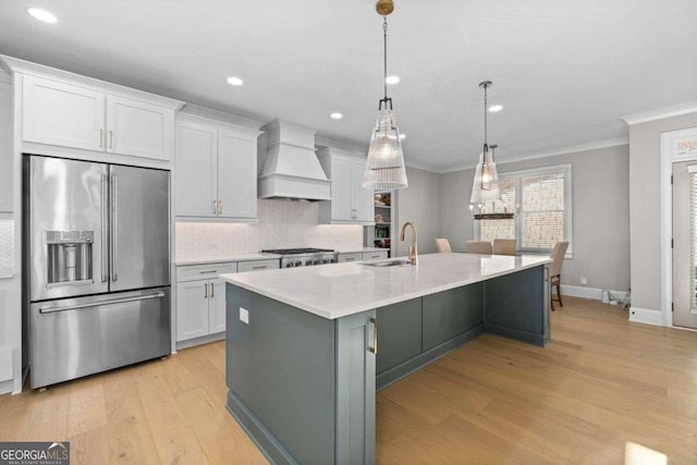 kitchen featuring a kitchen island with sink, white cabinets, hanging light fixtures, custom range hood, and stainless steel appliances