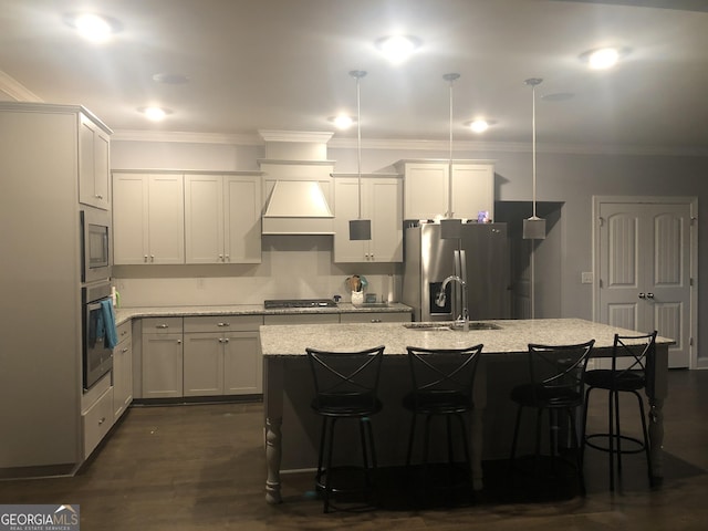 kitchen with appliances with stainless steel finishes, light stone countertops, hanging light fixtures, and a center island with sink