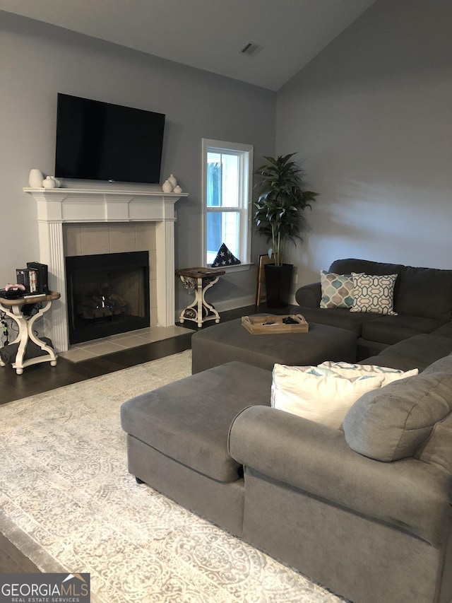 living room featuring a tile fireplace, lofted ceiling, and wood-type flooring