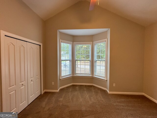 unfurnished bedroom with lofted ceiling with beams, dark colored carpet, a closet, and ceiling fan