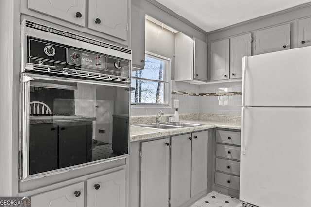 kitchen featuring sink, tasteful backsplash, white fridge, black oven, and white cabinets